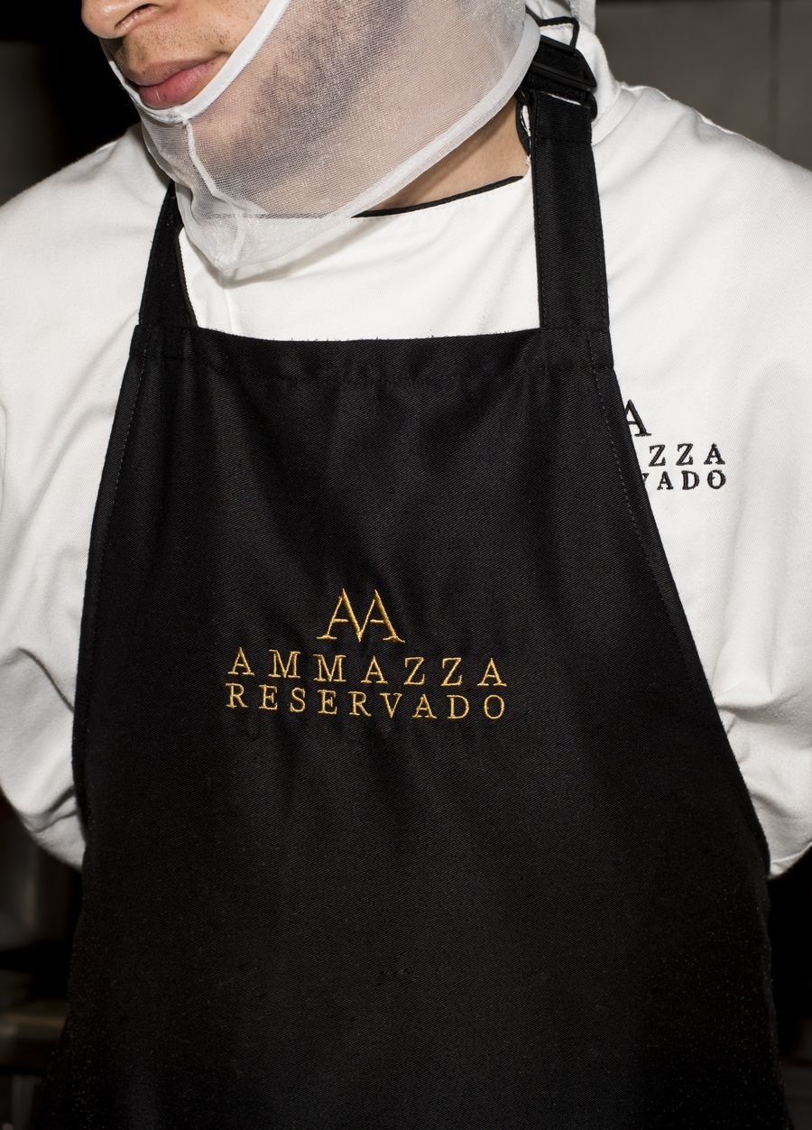 Detalle del logo bordado en dorado sobre un delantal negro